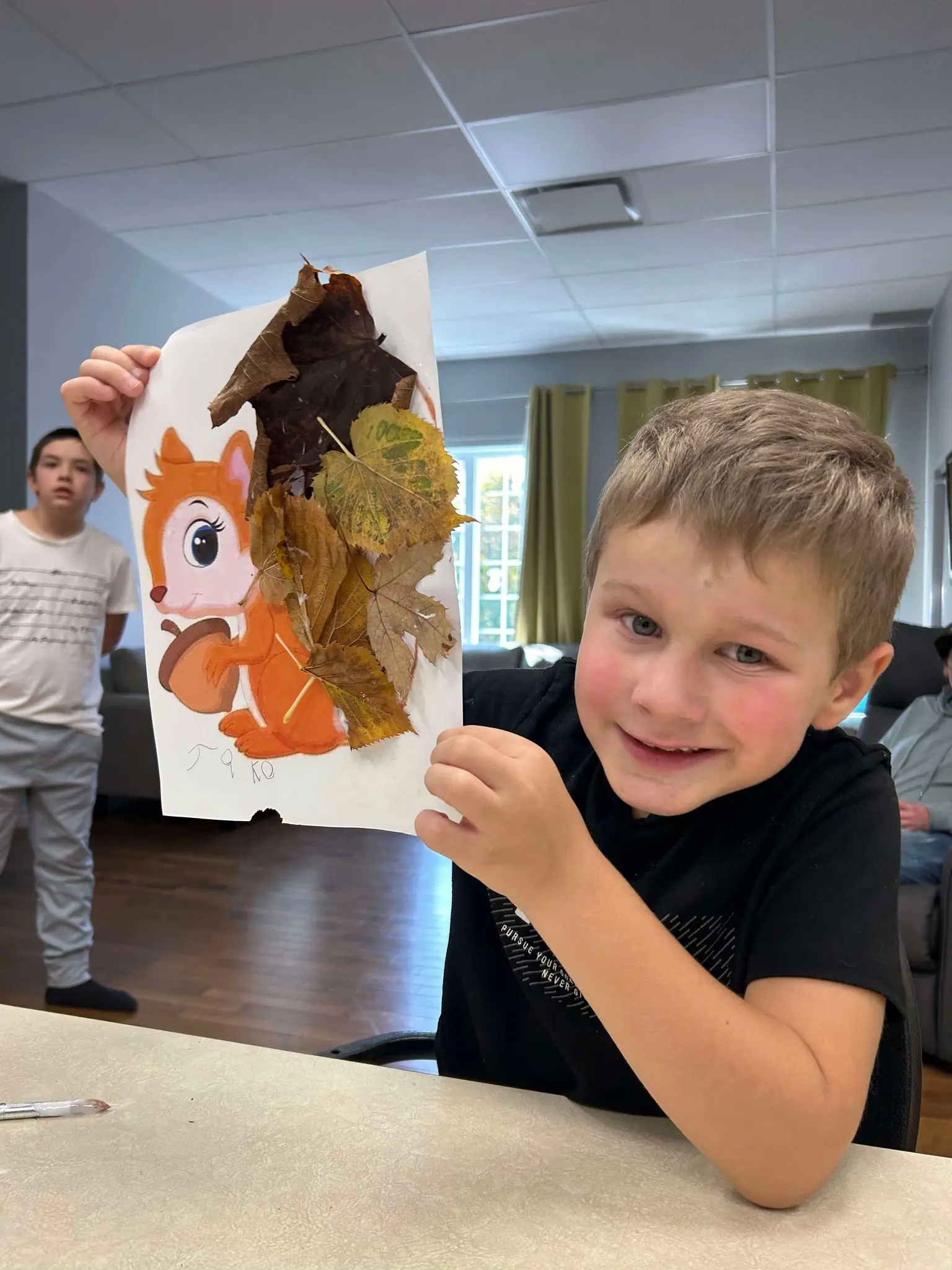 Garçon heureux de son bricolage d'une illustration écureuil avec la queue réalisée avec des feuilles d'arbres.